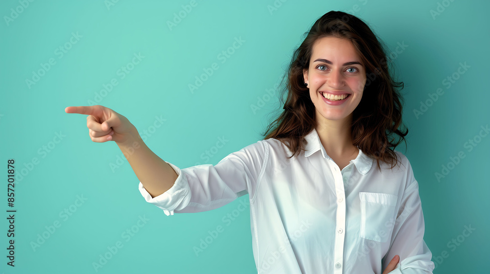 Smiling young woman pointing her finger, standing against a vibrant turquoise background Smiling young woman pointing her finger, standing against a vibrant turquoise background