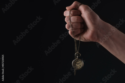 Man holding chain with elegant pocket watch on black background, closeup. Space for text