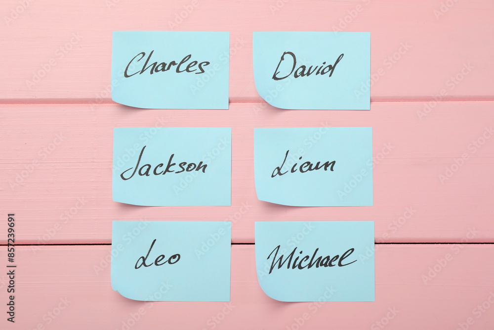 Paper stickers with different names on pink wooden background, flat lay. Choosing baby's name Paper stickers with different names on pink wooden background, flat lay. Choosing baby's name