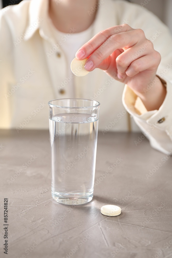 Woman putting effervescent pill into glass of water at grey table, closeup Woman putting effervescent pill into glass of water at grey table, closeup