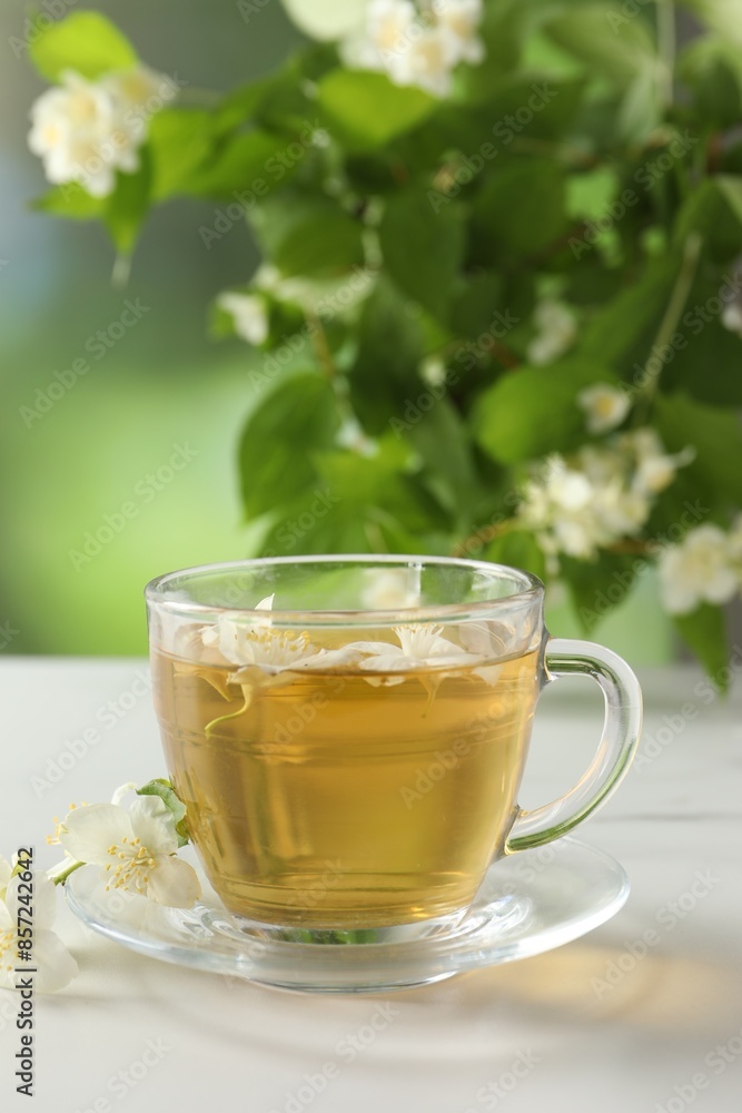 Aromatic jasmine tea in cup, flowers and green leaves on white table Aromatic jasmine tea in cup, flowers and green leaves on white table