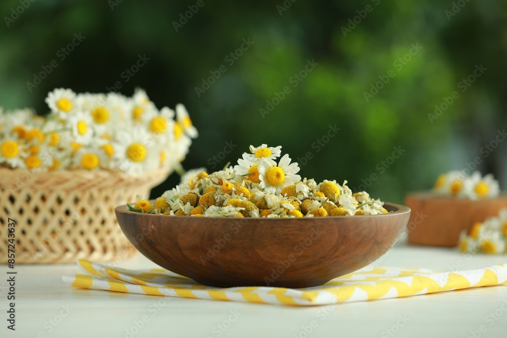 Dry and fresh chamomile flowers in bowl on light table against blurred green background Dry and fresh chamomile flowers in bowl on light table against blurred green background