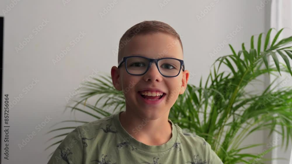 Teenager wearing glasses smiles a wide grin at the camera. Boy about 8 or 10 years old. Сhild emotions. Smile and joy. Close up. Slow motion. Boy against the greenery. 