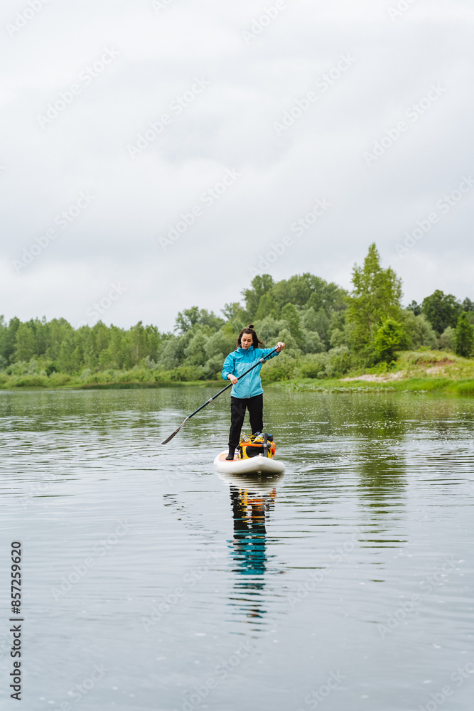 A tranquil scene of a woman paddle boarding in a lake under a cloudy sky, surrounded by boats and trees. The watercraft glides peacefully on the serene water, creating a calming setting A tranquil scene of a woman paddle boarding in a lake under a cloudy sky, surrounded by boats and trees. The watercraft glides peacefully on the serene water, creating a calming setting