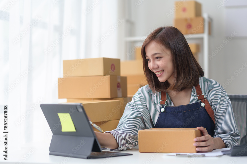 Smiling woman working on a laptop, surrounded by cardboard boxes, handling packaging for her online business or e-commerce store. Smiling woman working on a laptop, surrounded by cardboard boxes, handling packaging for her online business or e-commerce store.