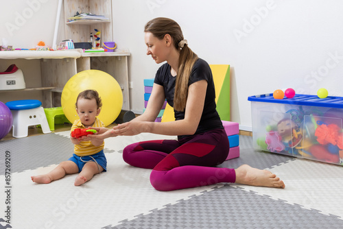 Skilled physical therapist engaging with child during physical rehabilitation session sitting in gym mat in medical center