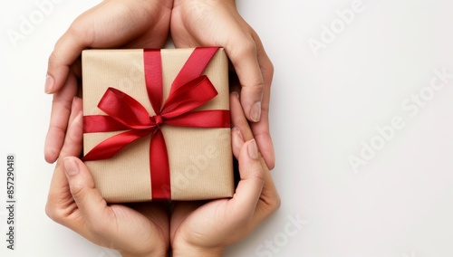 A close-up shot of two hands holding a gift box wrapped in brown paper with a red bow on a white background