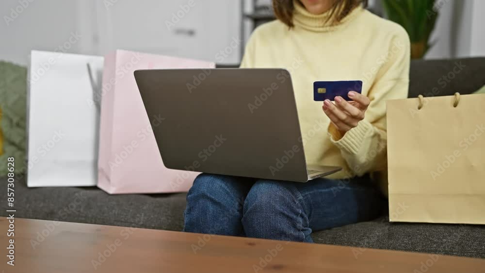 A young woman shops online with a credit card and laptop at home, amidst shopping bags. A young woman shops online with a credit card and laptop at home, amidst shopping bags.