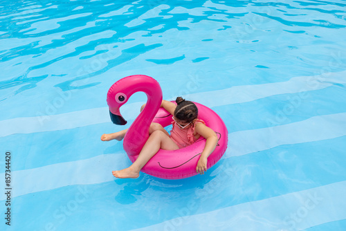 Cute little girl lying on inflatable swimming ring flamingo in swimming pool with blue water on warm summer day on tropical vacations. Summertime activities concept. sunbathing on the sun. Top view photo