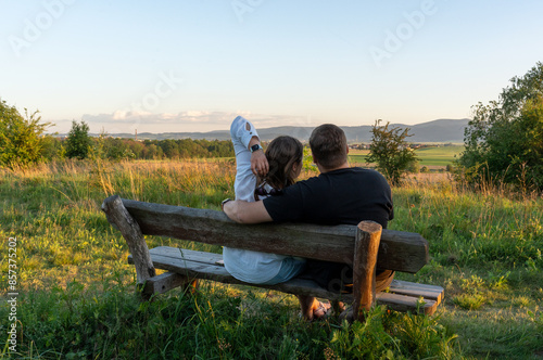 Happy couple of man and woman sitting on a park bench on a summer day at sunset. The view of the mountains and the field. Love and relationships. Psychology of family. . High quality photo