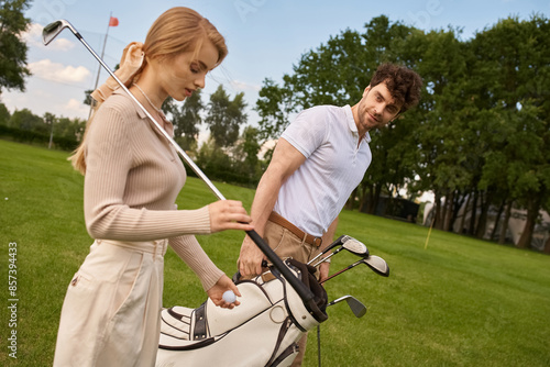 A man and woman in elegant attire stand together on a lush golf course, embodying a refined display of leisure and sophistication. photo