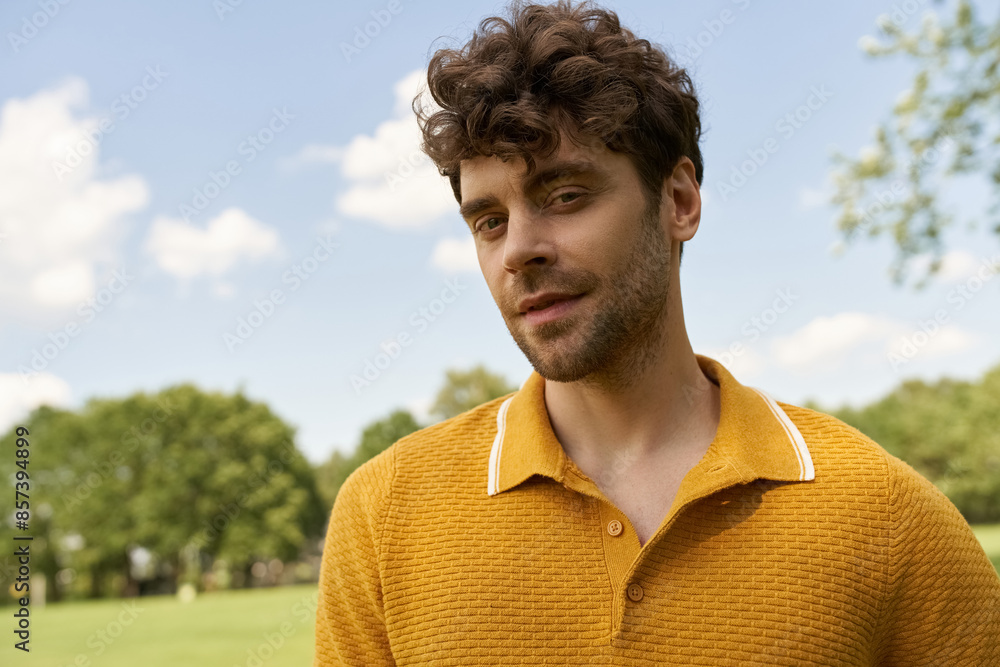 A stylish man in a vibrant yellow shirt stands amidst the lush greenery of a park on a sunny day. A stylish man in a vibrant yellow shirt stands amidst the lush greenery of a park on a sunny day.