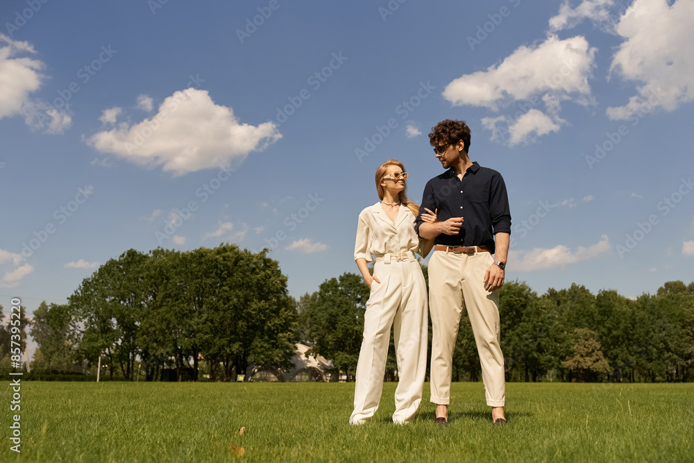 A stylish young man and woman clad in elegant attire are standing side by side on a lush green field. A stylish young man and woman clad in elegant attire are standing side by side on a lush green field.