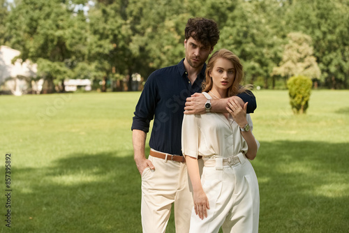 Elegant couple in fashionable attire enjoying a day at the park surrounded by lush greenery.