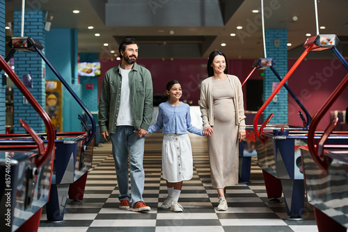 A happy family is joyfully walking through a air hockey in a mall during the weekend, enjoying a day of fun together.