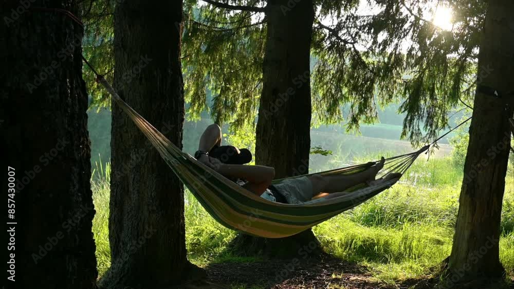 A man relaxes lying in a hammock, in a beautiful landscape, on the shore of the lake, among the trees. In camping, in nature. A man relaxes lying in a hammock, in a beautiful landscape, on the shore of the lake, among the trees. In camping, in nature.