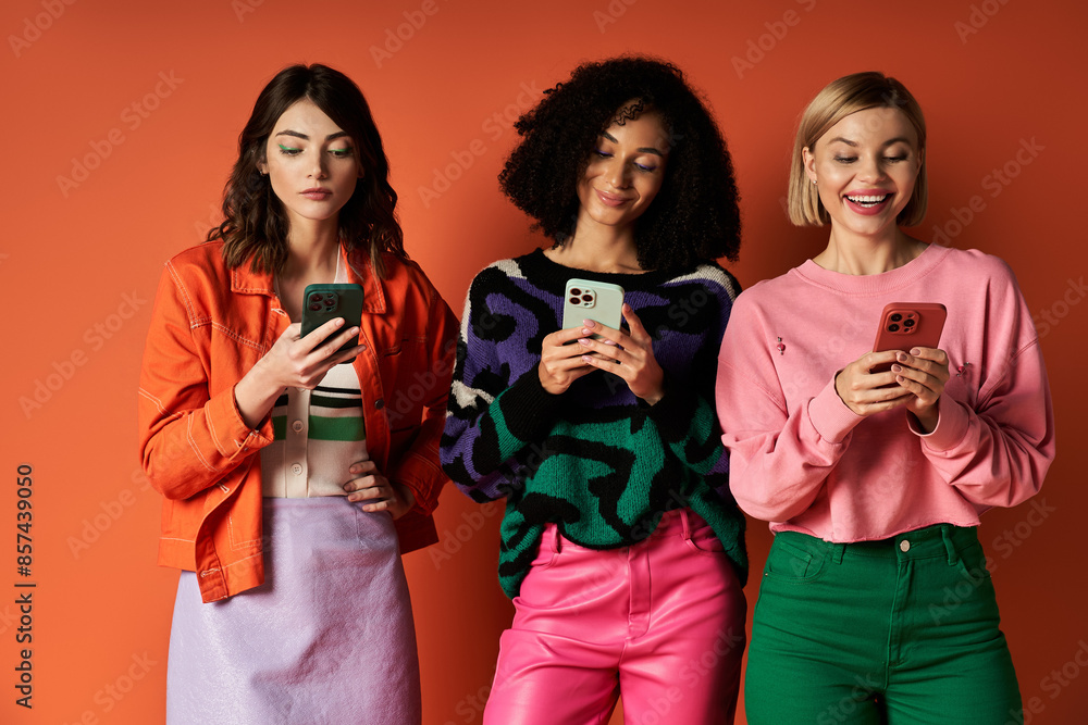 Three young, beautiful women in stylish clothes, displaying diversity in culture, pose together against an orange background. Three young, beautiful women in stylish clothes, displaying diversity in culture, pose together against an orange background.