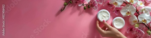 White Orchid Flowers and a Hand With Manicured Nails on a Pink Background