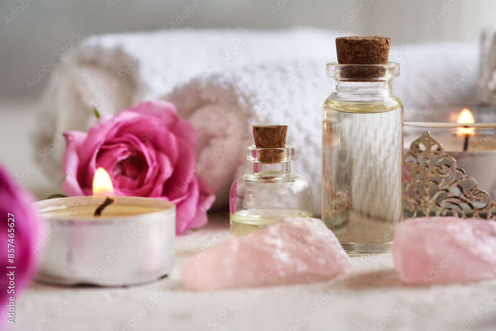 Two bottles of aromatherapy essential oil with rose de Mai flowers, rose quartz stones and spa towels Two bottles of aromatherapy essential oil with rose de Mai flowers, rose quartz stones and spa towels