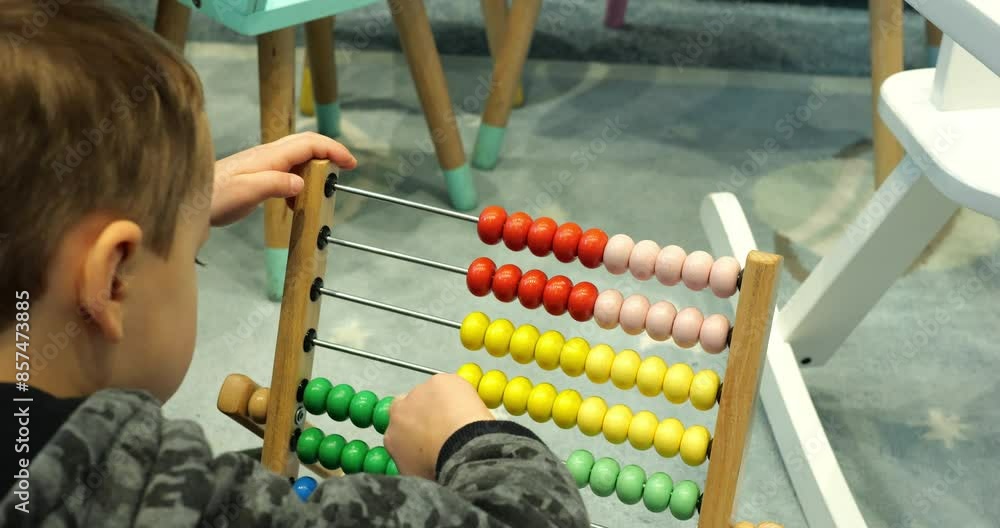 Smart little student moves wooden beads of counting frame in kindergarten room closeup. Toddler child boy learns adding with vintage abacus in classroom
