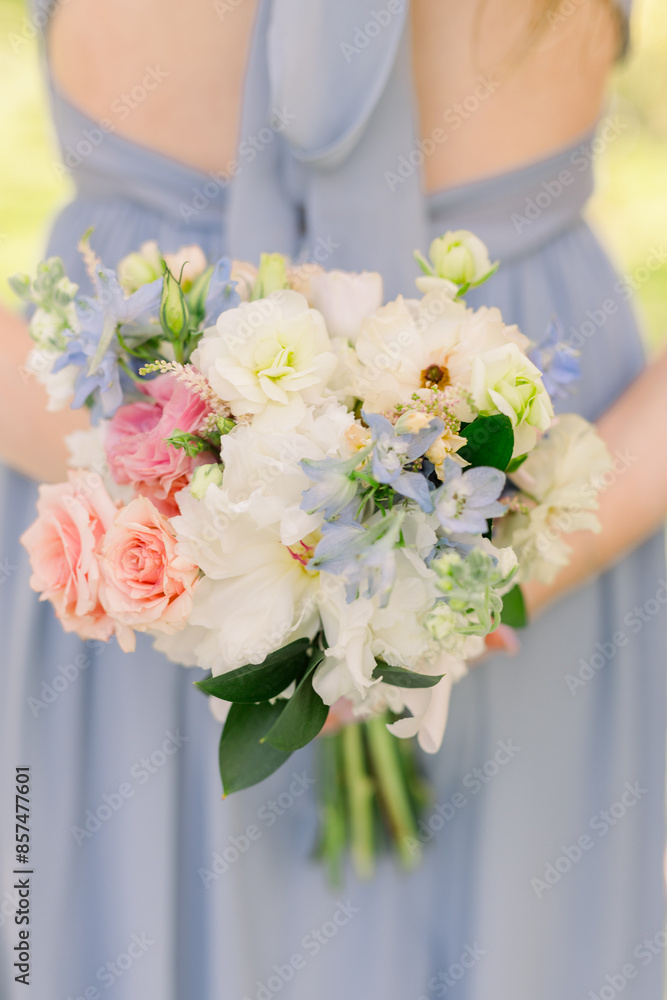 Bridesmaid in a light blue dress holding floral arrangement behind her back. Bridesmaid in a light blue dress holding floral arrangement behind her back.