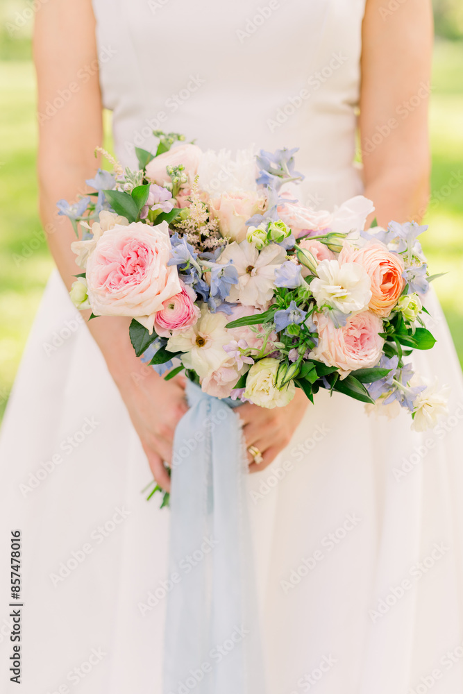 A bride is holding a summer pink summer bouquet with blue ribbon. A bride is holding a summer pink summer bouquet with blue ribbon.