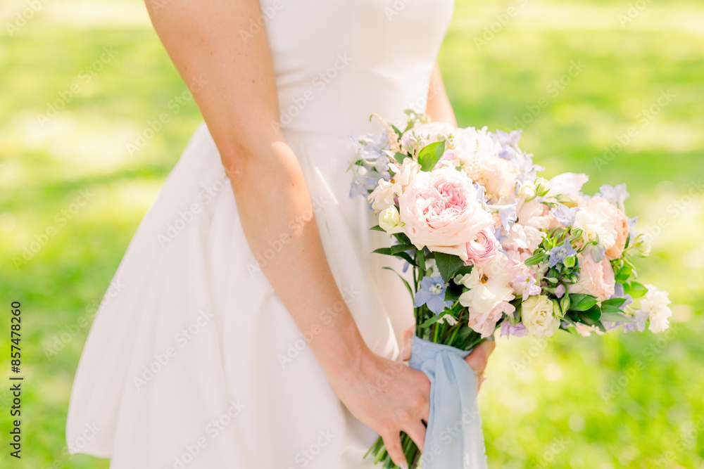 A bride is holding a beautiful pink bouquet and light blue ribbon. 
