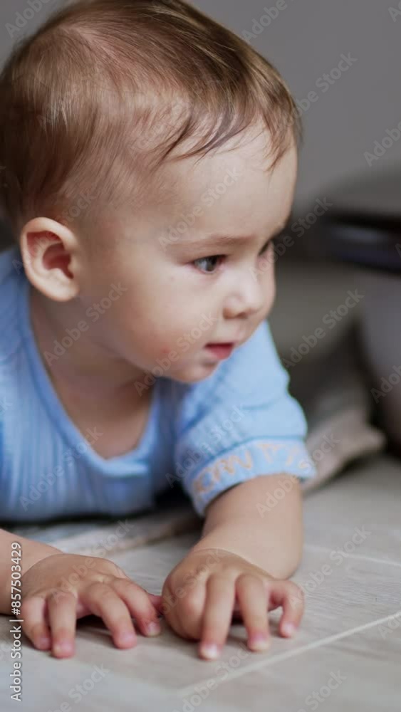 Nice cute child lies on the floor watching the ball rolling in front of him. Little boy crawling up to the toy watching it move. Close up. Vertical video Nice cute child lies on the floor watching the ball rolling in front of him. Little boy crawling up to the toy watching it move. Close up. Vertical video