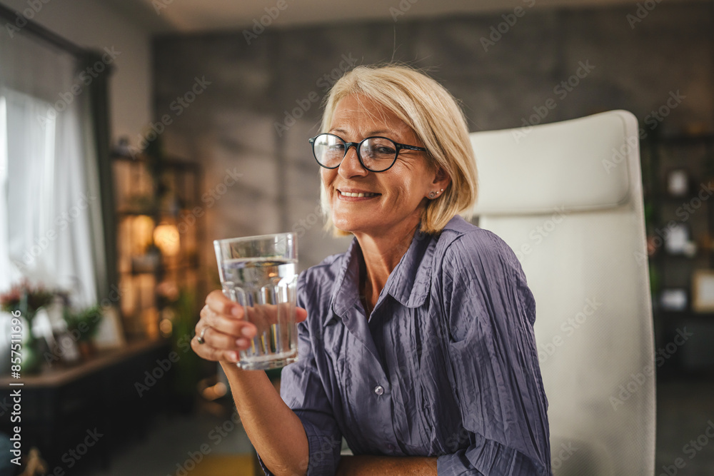 Portrait of mature woman sit, smile and hold glass of water at home Portrait of mature woman sit, smile and hold glass of water at home