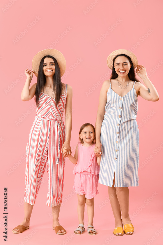 Young lesbian couple with adopted little girl holding hands on pink background Young lesbian couple with adopted little girl holding hands on pink background