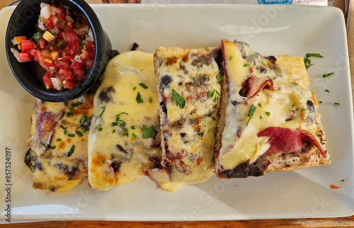 A plate of food called molletes with a white plate and a black bowl. The food is a cheese and meat dish, mexico photo