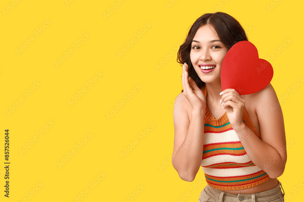 Happy young Asian woman with red paper heart on yellow background. Valentine's Day celebration Happy young Asian woman with red paper heart on yellow background. Valentine's Day celebration