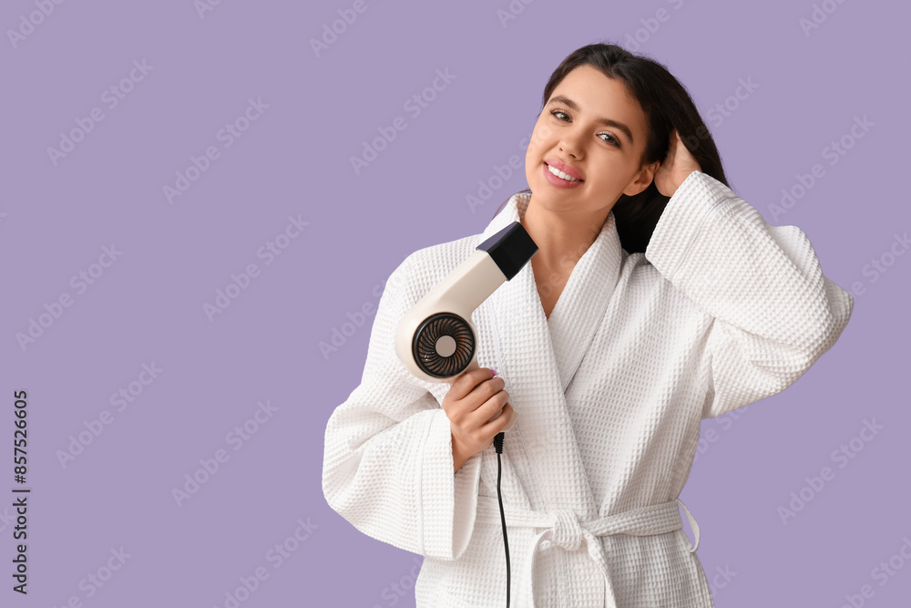 Beautiful young happy woman in bathrobe with hair dryer on purple background Beautiful young happy woman in bathrobe with hair dryer on purple background