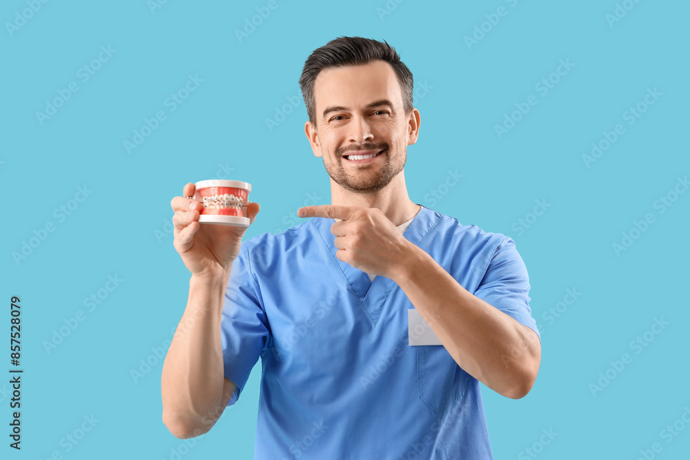Portrait of male dentist pointing at jaw model on blue background Portrait of male dentist pointing at jaw model on blue background
