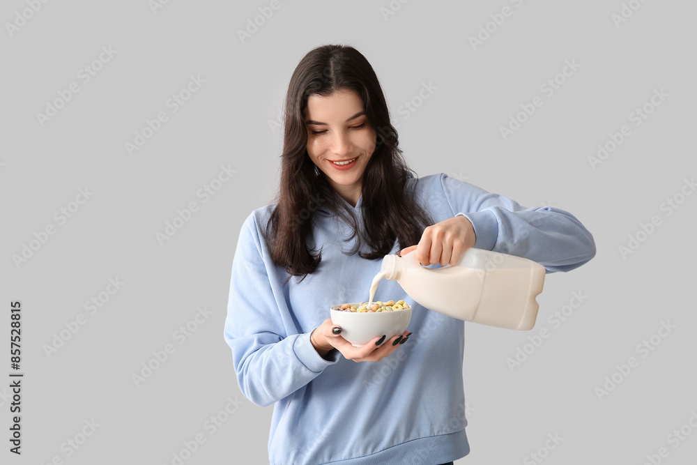 Young woman pouring milk into bowl of tasty cereal rings on light background Young woman pouring milk into bowl of tasty cereal rings on light background