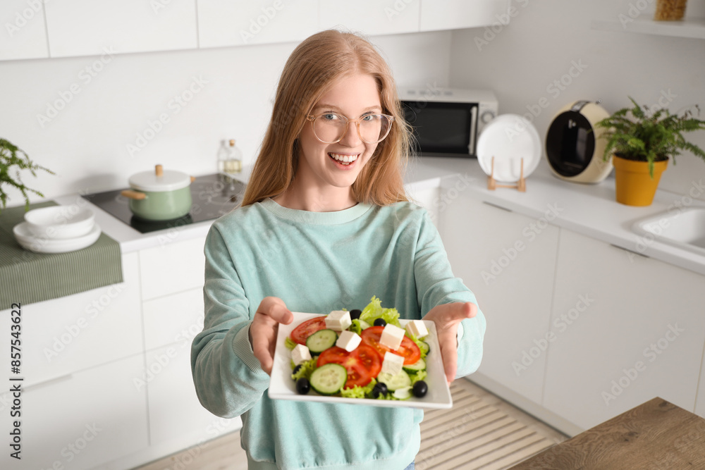 Happy young woman holding plate of tasty salad with feta cheese in kitchen Happy young woman holding plate of tasty salad with feta cheese in kitchen