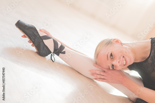 A young woman lies bent over on her feet in a ballet class. Ballerina stretches on the floor.  photo