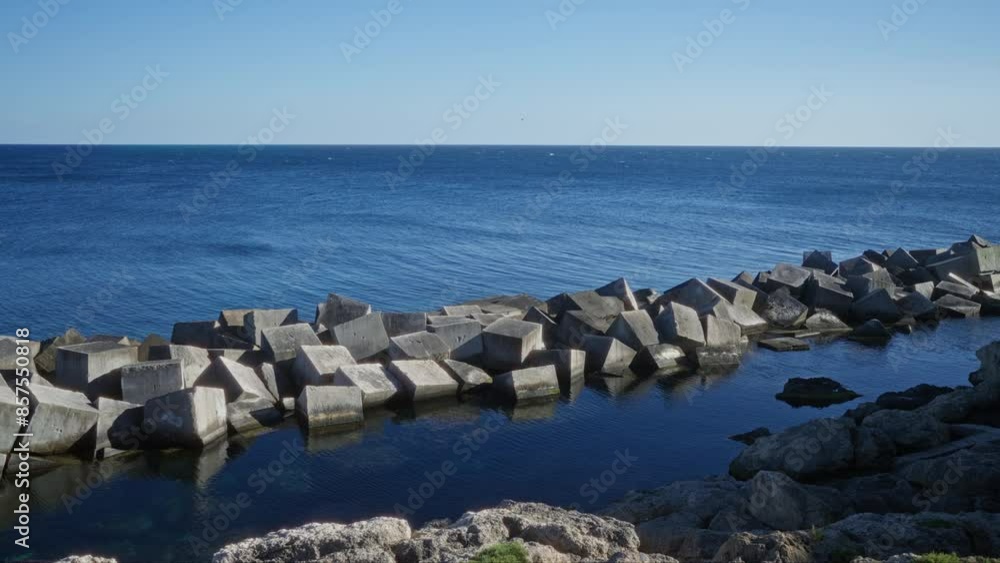 Concrete blocks on the coastline of gallipoli, puglia, italy, under a clear sky with serene blue sea and rocky shore in the background. Concrete blocks on the coastline of gallipoli, puglia, italy, under a clear sky with serene blue sea and rocky shore in the background.