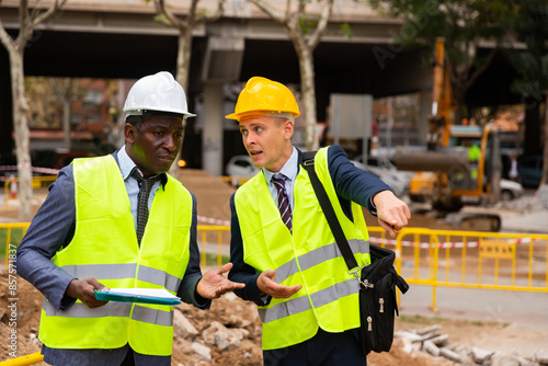 Engineer and architect are discussing options for laying a pipe on the street