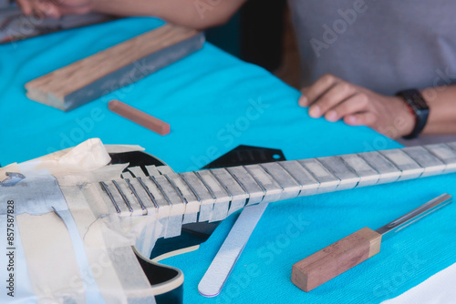 Fotografie Black electric guitar in repair shop with the hands of a guitar luthier fixing it, frets alignment