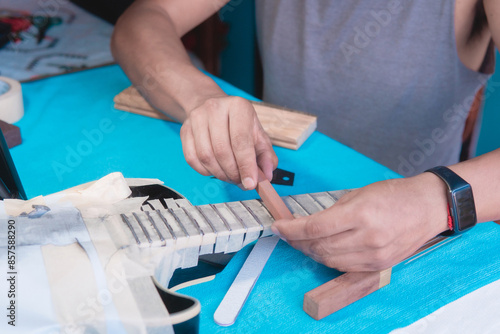 Black electric guitar in repair shop with the hands of a guitar luthier fixing it, frets alignment.