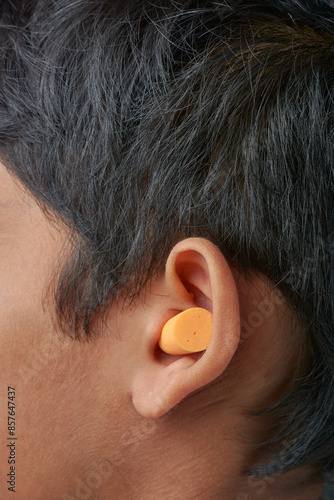 disposable soft expandable foam earplugs inserted into ear, wearing single use uncorded and comfortable hearing protection used in workplace, concerts and sleeping, selective focus with copy space