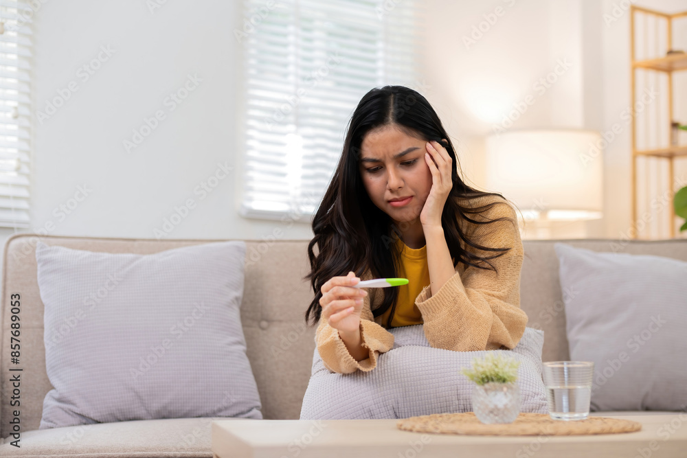 Woman Sitting on Couch Holding Pregnancy Test with Worried Expression in Bright Living Room Woman Sitting on Couch Holding Pregnancy Test with Worried Expression in Bright Living Room