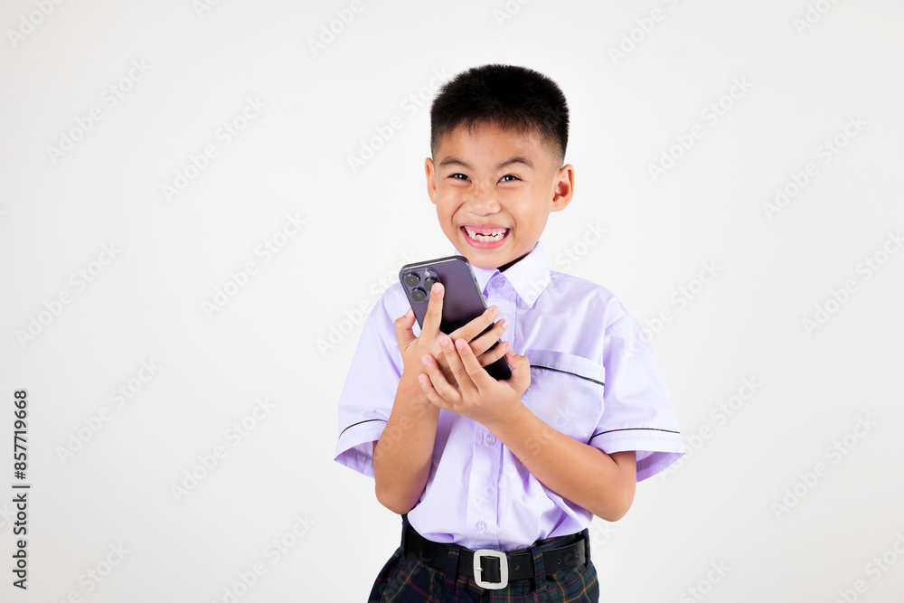 Portrait smiling Asian little boy primary posing holding a cell phone studio isolated white background, happy cute man kid wear school uniform hold smartphone enjoying himself, back to school concept Portrait smiling Asian little boy primary posing holding a cell phone studio isolated white background, happy cute man kid wear school uniform hold smartphone enjoying himself, back to school concept