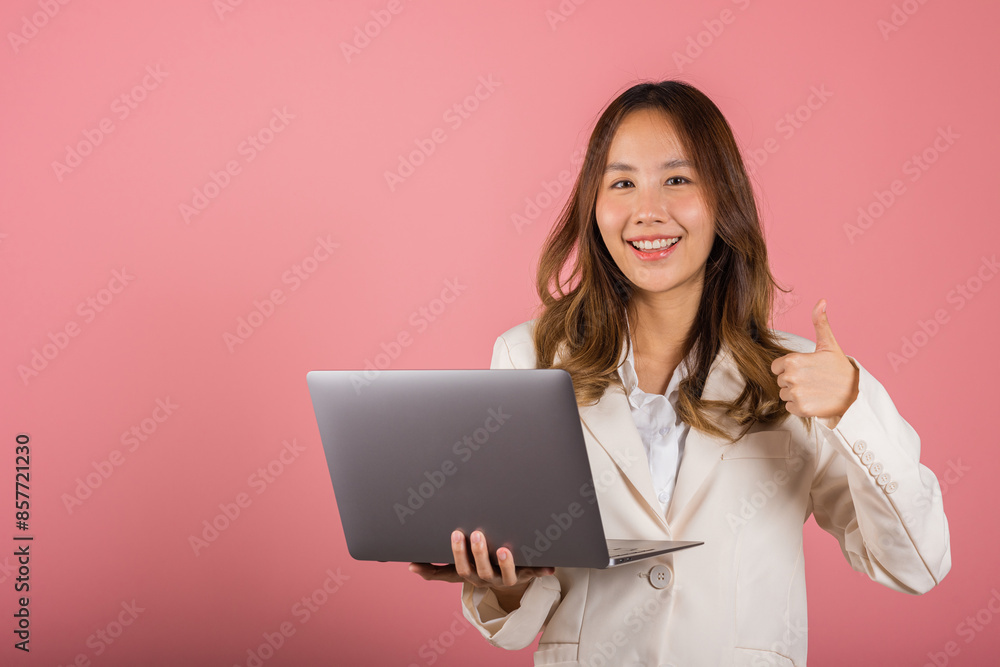 Portrait of happy Asian beautiful business woman confident smiling face holding using laptop computer and showing thumb up for like gesture, studio shot with copy space isolated on pink background Portrait of happy Asian beautiful business woman confident smiling face holding using laptop computer and showing thumb up for like gesture, studio shot with copy space isolated on pink background