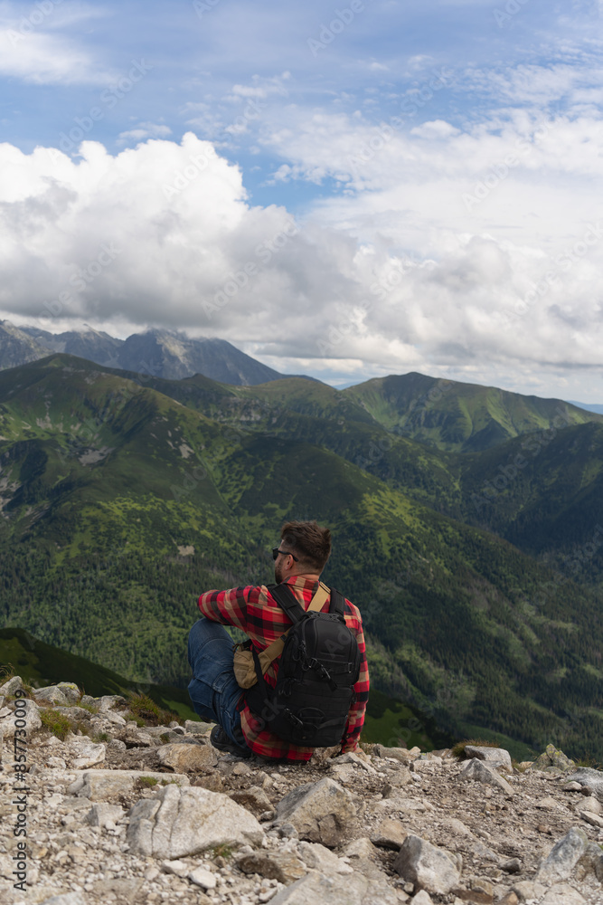 A man high in the Polish Tatra Mountains sits on a cliff on a summer day, photo from behind. A man high in the Polish Tatra Mountains sits on a cliff on a summer day, photo from behind.