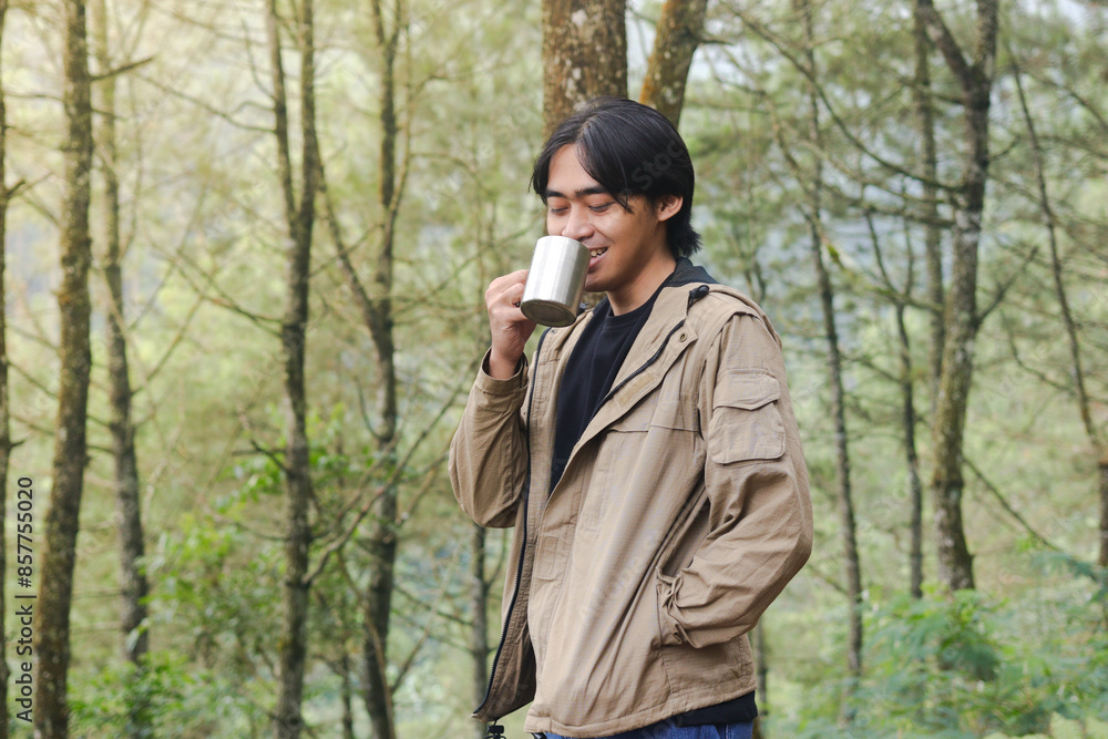 Portrait of excited Asian hiker man drinking water from stainless steel cup while trekking in nature forest Portrait of excited Asian hiker man drinking water from stainless steel cup while trekking in nature forest