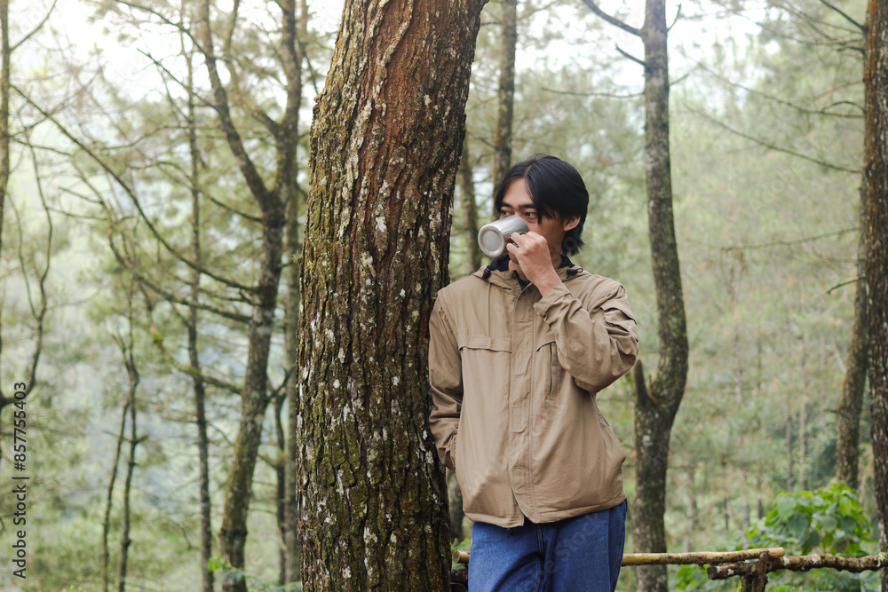 Portrait of excited Asian hiker man drinking water from stainless steel cup while trekking in nature forest Portrait of excited Asian hiker man drinking water from stainless steel cup while trekking in nature forest