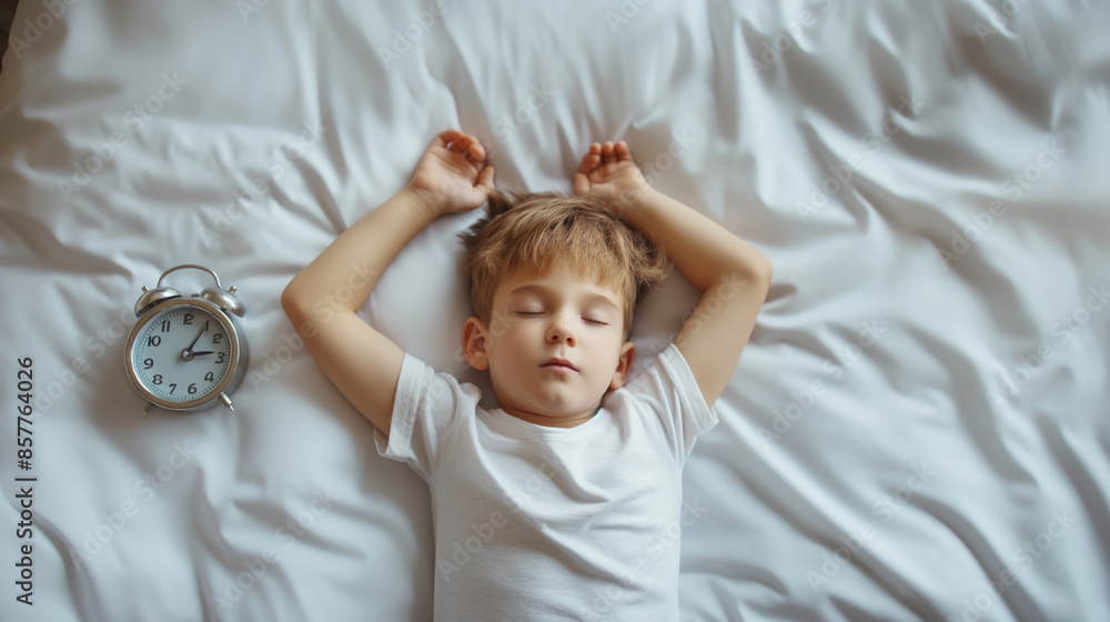 Fototapeta premium Little boy sleeping in white bed with alarm clock