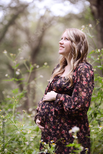 Smiling pregnant woman in a floral dress standing in a serene wo photo